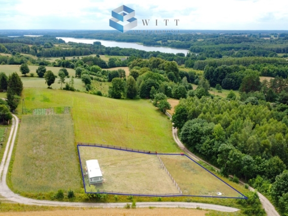 Widok na działkę budowlaną z domem w otoczeniu zieleni, z widokiem na rzekę i okoliczne tereny.