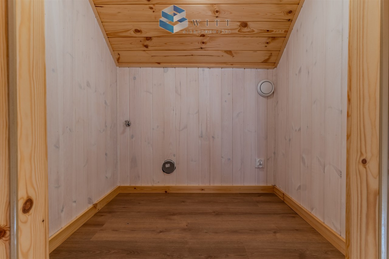 Pusty pokój z drewnianymi ścianami i podłogą, z widocznymi gniazdkami elektrycznymi i wentylacją.