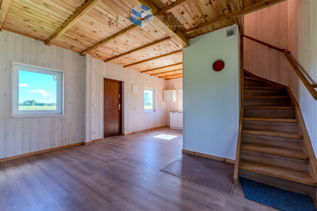 Wnętrze nowoczesnego domu z drewnianymi elementami, widok na schody oraz okno z widokiem na zewnątrz.