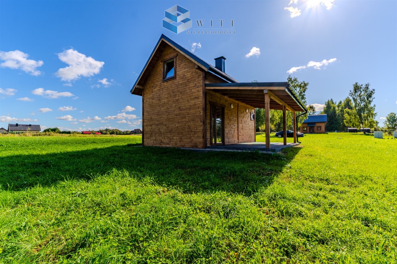 Nowoczesny dom z drewnianą elewacją, umiejscowiony na zielonej działce, w otoczeniu natury i błękitnego nieba.