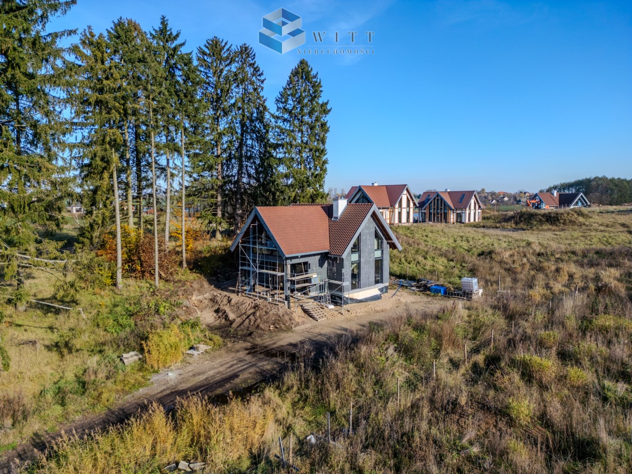 Dom w budowie otoczony drzewami, z widokiem na inne budynki, na tle nieba.