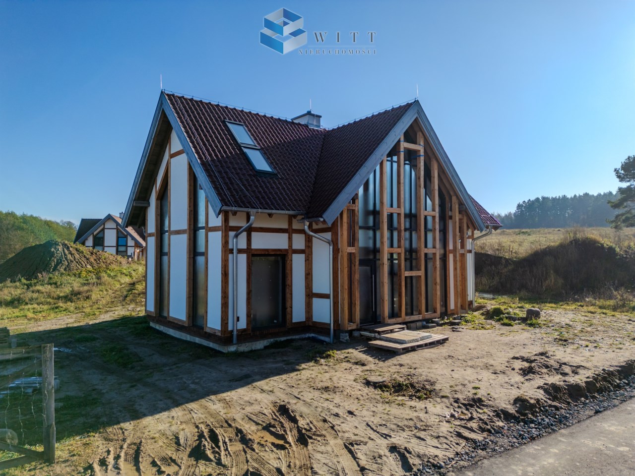 Nowoczesny dom jednorodzinny z drewnianą konstrukcją, dużymi oknami i dachem dwuspadowym, otoczony zielenią i naturalnym krajobrazem.