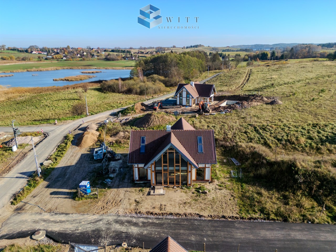 Widok na nowe domy w trakcie budowy w malowniczej okolicy, z widokiem na jezioro i zielone tereny.