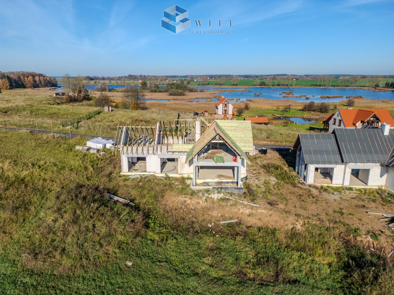 Widok z lotu ptaka na budowę domów w malowniczej okolicy z jeziorami i zielonymi terenami.