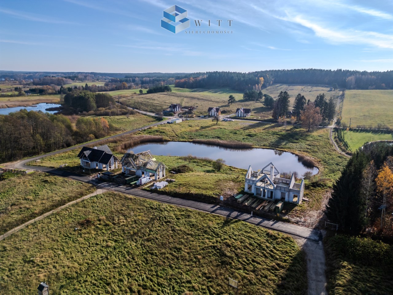 Widok z lotu ptaka na teren budowy domów w malowniczej okolicy z jeziorami i zielonymi łąkami.