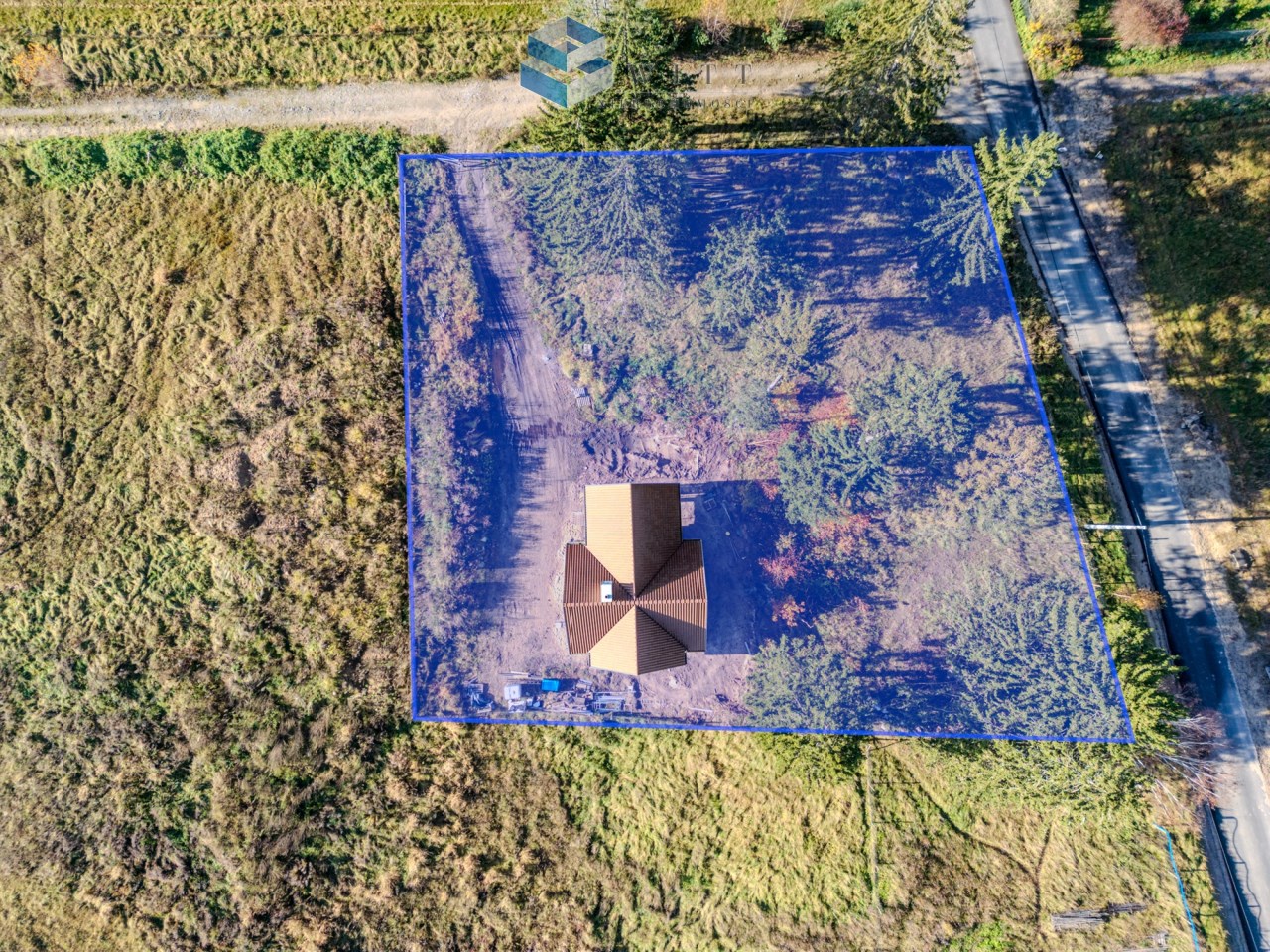 Widok z góry na dom otoczony działką z zielenią i drogą w tle, z zaznaczeniem obszaru w niebieskiej ramce.