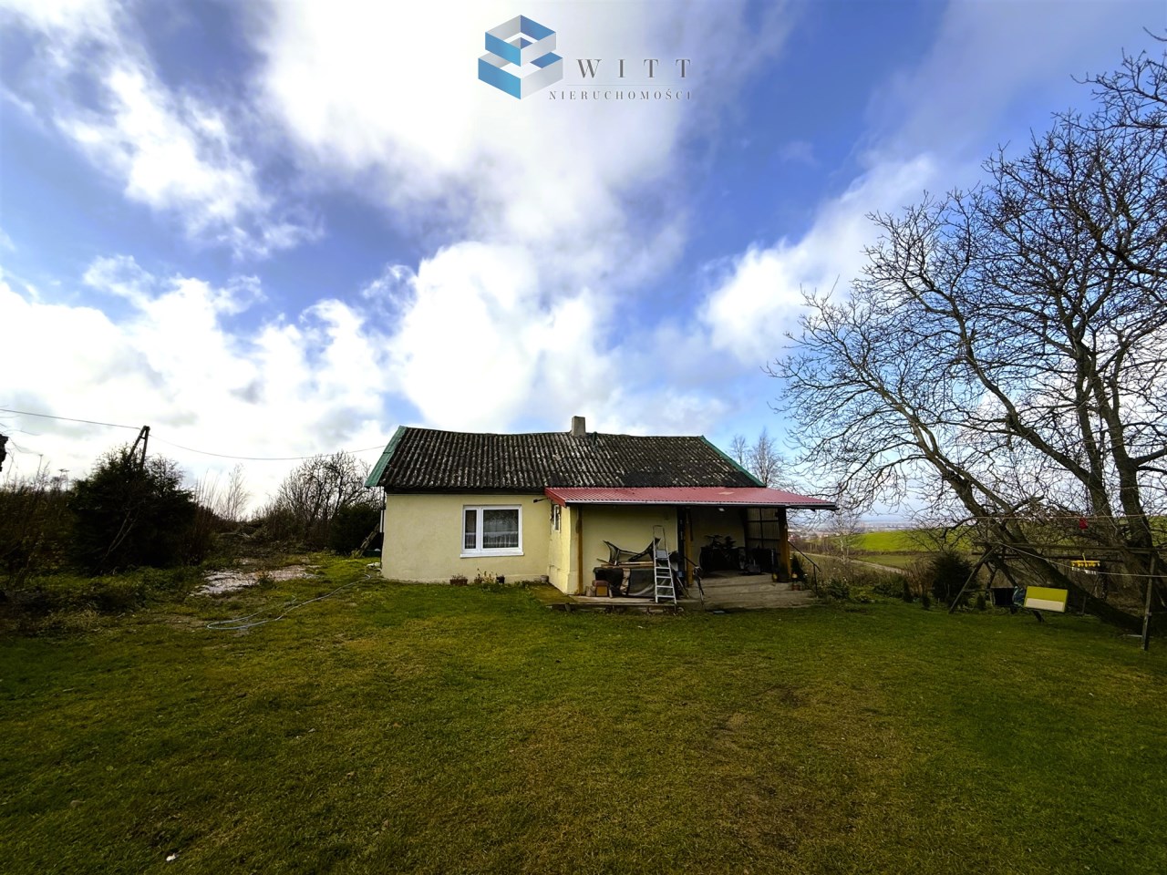 Dom jednorodzinny z ogrodem, widok na niebo i otaczającą przyrodę, w tle drzewa i trawa.