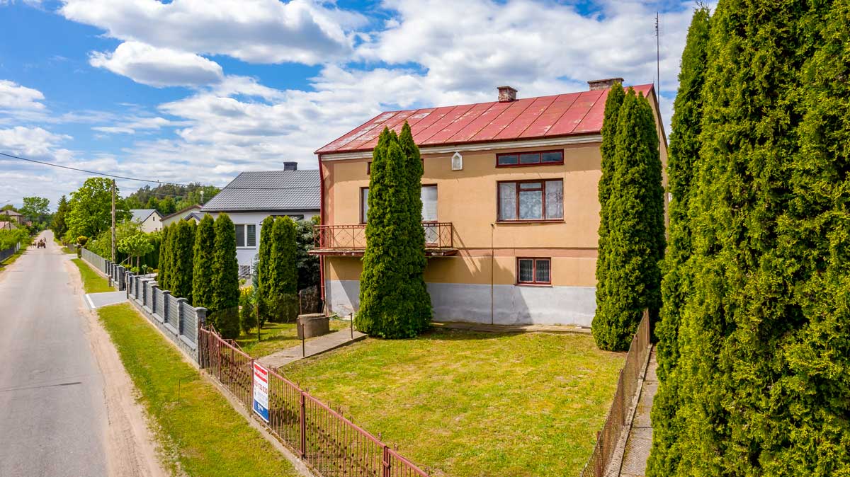 570997465_2735070770172526_971247030504723120_n Widok na dom z czerwonym dachem otoczony wysokimi cyprysami, położony przy spokojnej ulicy. W tle widać inne budynki mieszkalne oraz zieleń. Idealne miejsce na rodzinny dom.