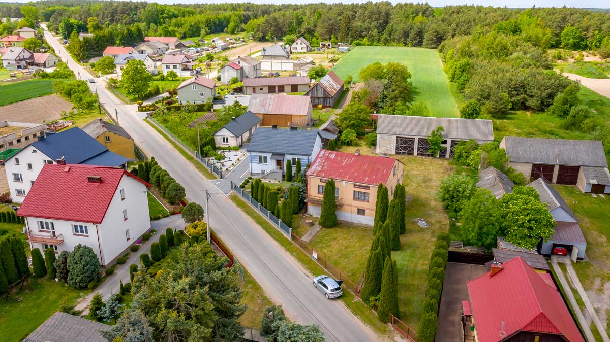 571350885_2735070870172516_8471509254082088443_n Widok z lotu ptaka na wiejską okolicę z domami, drogami i zielonymi polami, otoczony lasami.