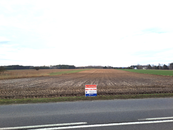 Pole na sprzedaż z widokiem na wiejskie tereny, z oznaczeniem kontaktowym na tablicy.