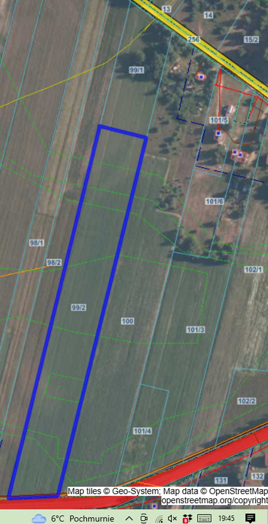 Mapa terenu z oznaczeniami działek, w tym niebieskie kontury obszarów oraz numery działek. W tle widoczne pola uprawne i elementy zabudowy.