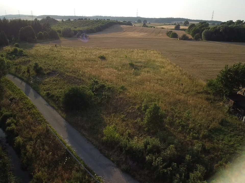 Widok na działkę o powierzchni 7 600 m² w Kłaczynie, Dobromierz, z widoczną drogą oraz otaczającymi ją polami i zalesieniem.